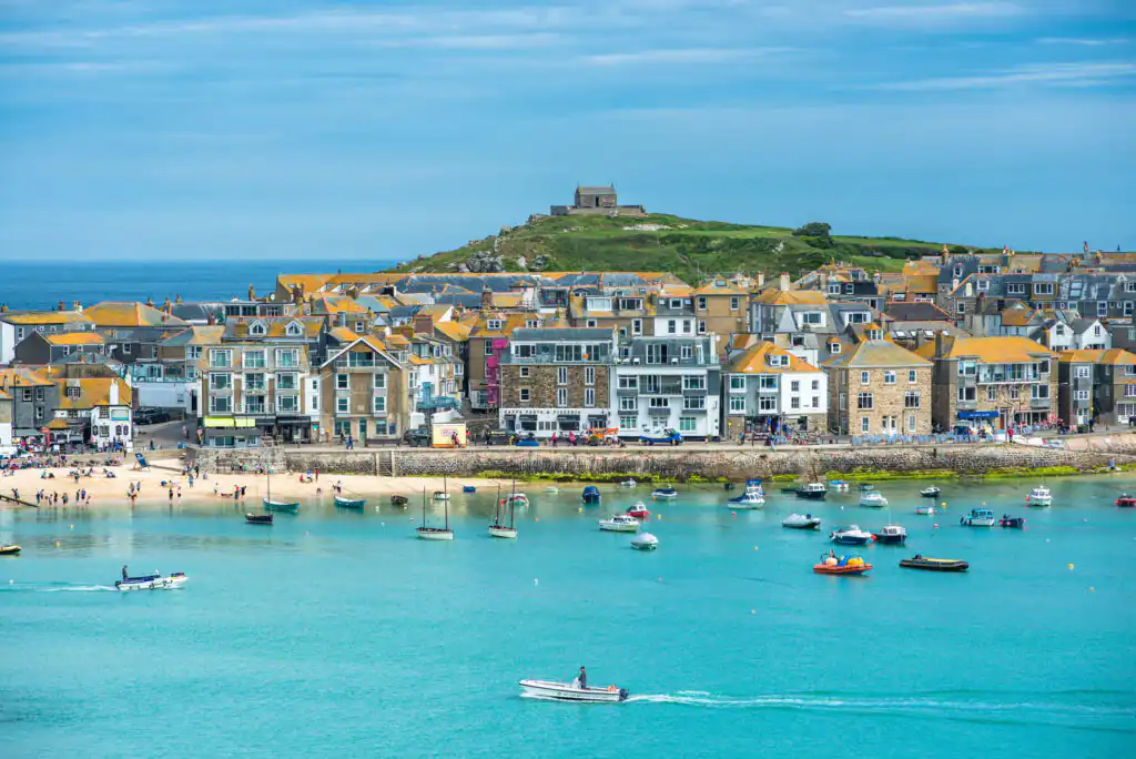St Ives Harbour with boats on turquoise water, a sandy beach with people, and colourful buildings, featuring Cintra, one of the best restaurants in St Ives.