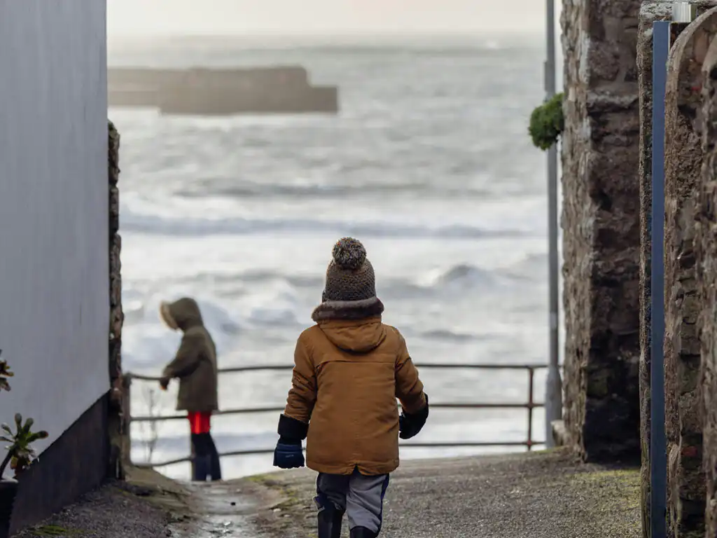 A child walks along a narrow path by the ocean, enjoying the scenic views of Mounts Bay in Marazion.