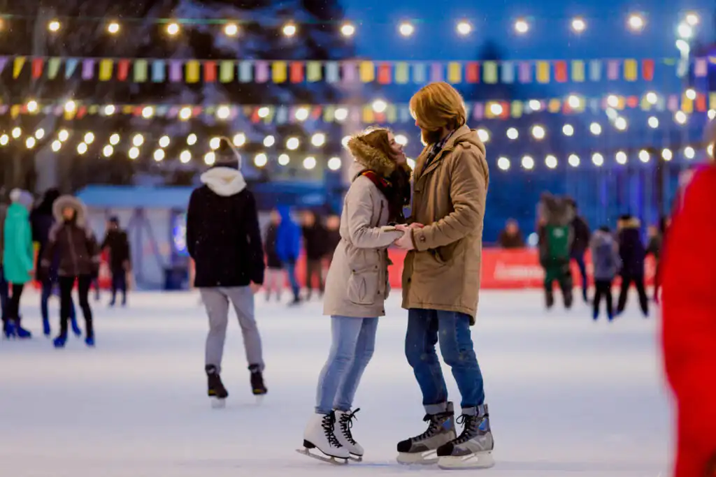 A couple ice skating under twinkling lights in Cornwall, capturing the festive spirit of Christmas at night.