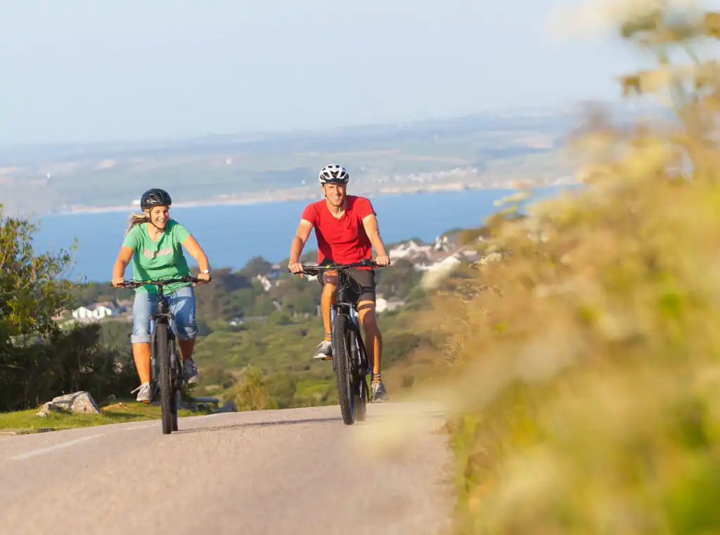 Two cyclists enjoying a scenic ride on a road in Cornwall, a great outdoor thing to do this September and October.
