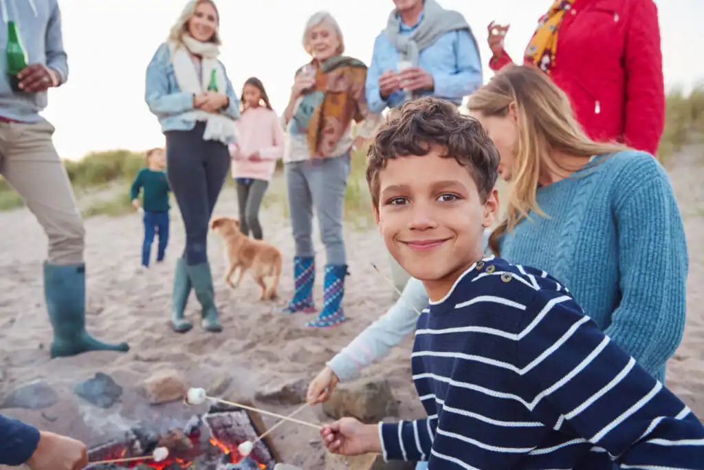 A family gathers around a campfire on the beach in Cornwall, a great activity for a large group holiday in Cornwall.