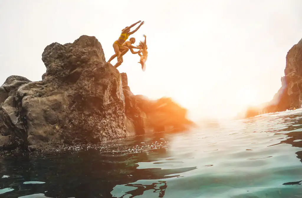 A family joyfully jumps from a cliff into the sea, showcasing the thrill of adventure in Cornwall's beautiful coastline.