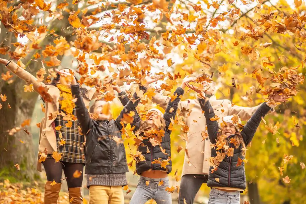 A family joyfully throws colourful leaves in the air in a lush forest during October half term in Cornwall.