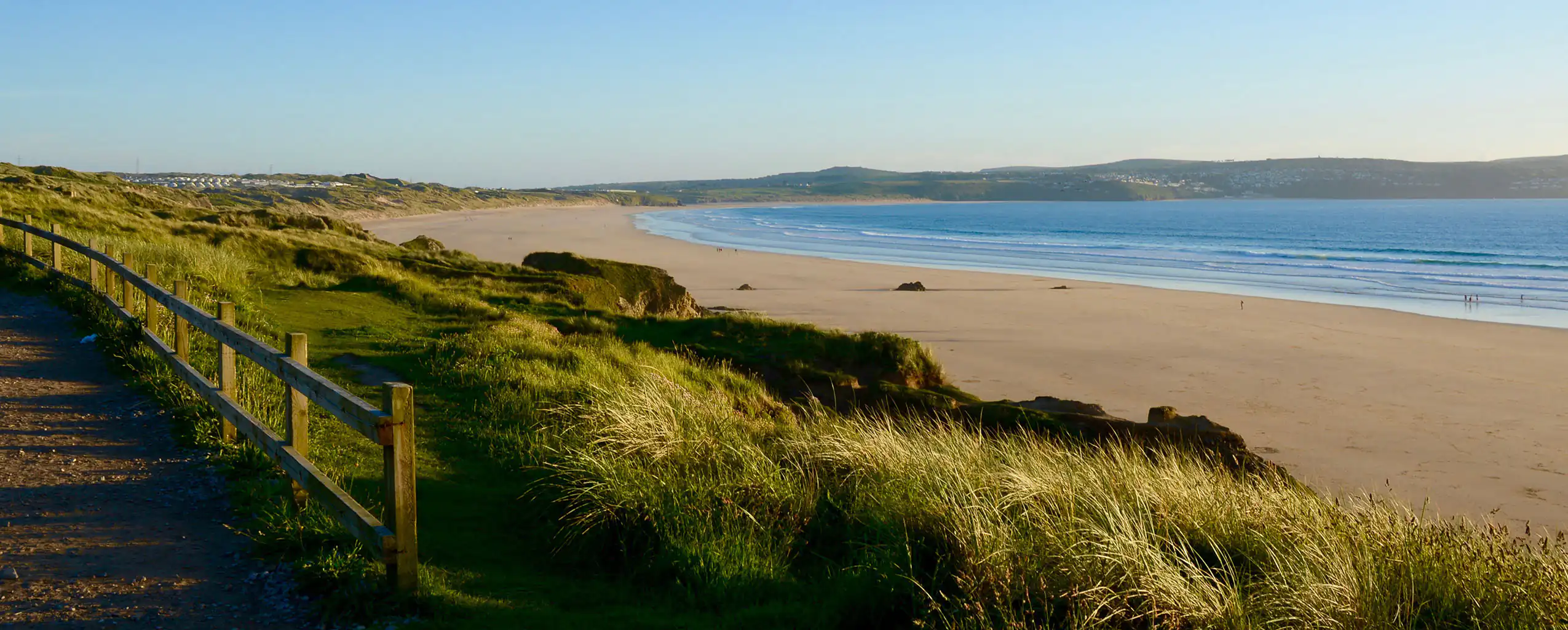 A footpath leading to the sandy shores of Gwithian Beach in Hayle, framed by grass and dunes, a great place to start a Hayle food adventure.