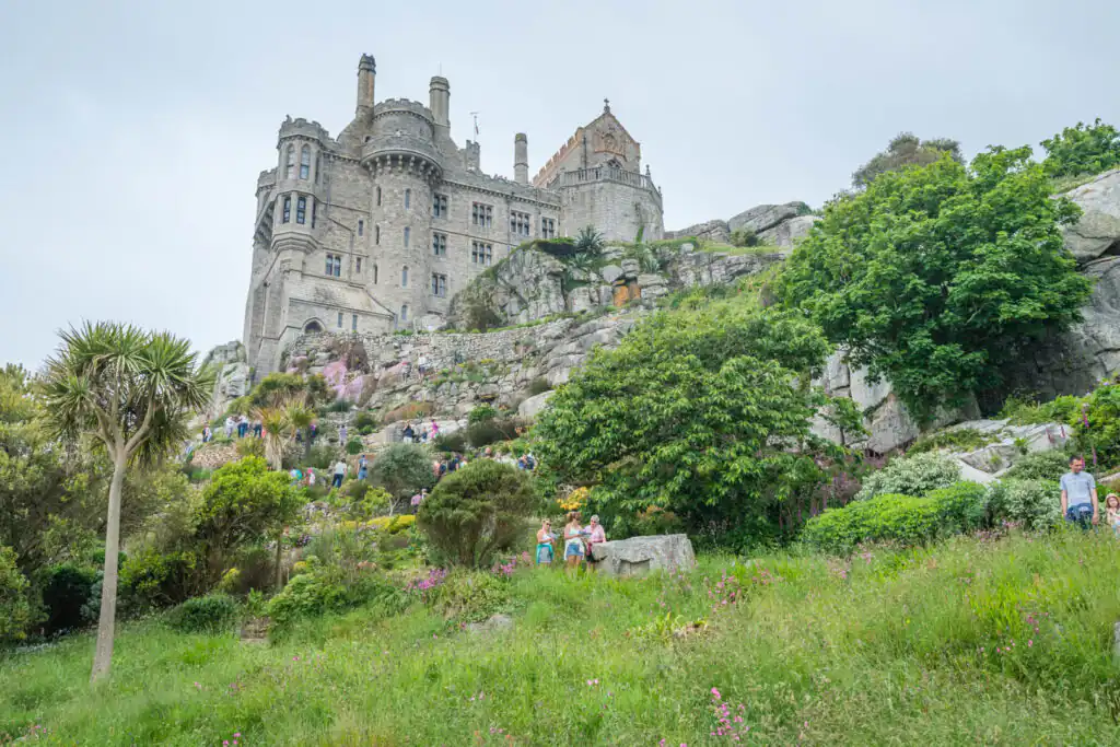 People walking up a hill surrounded by gardens, approaching the historic St Michael's Mount castle, one of the best gardens in Cornwall.