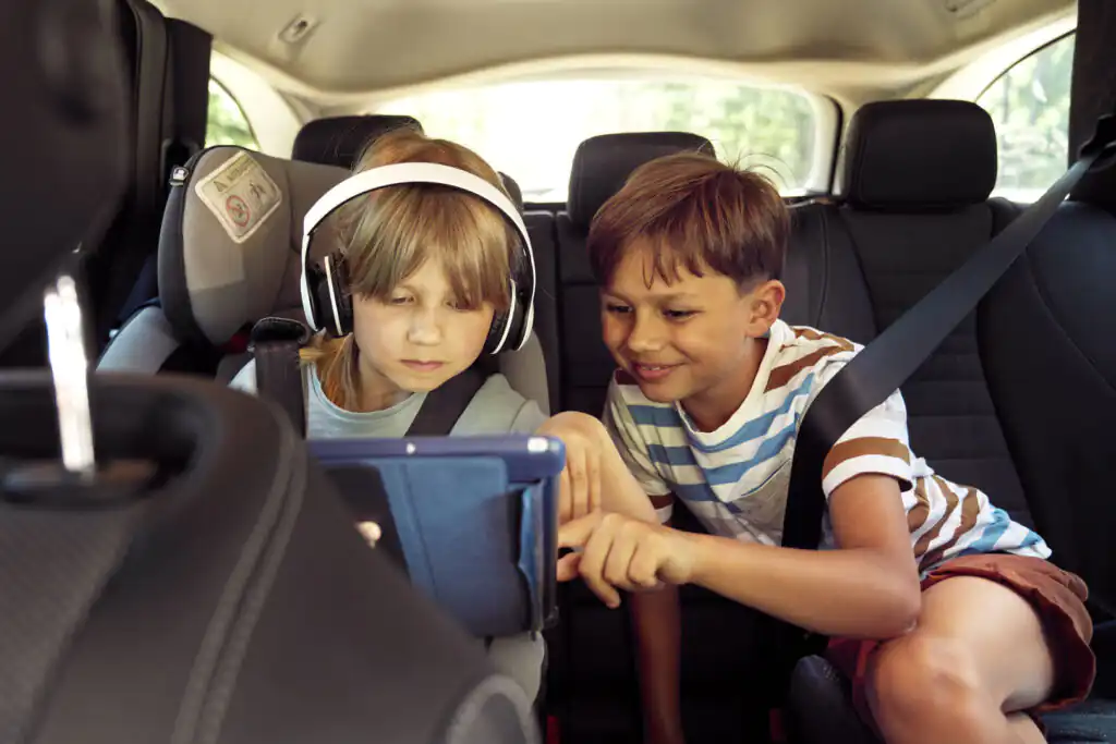 Two children in a car playing on a tablet, on their journey to Cornwall.