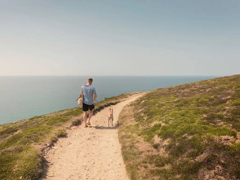 A man walks his dog along a scenic path by the ocean near Bedruthan Steps in Mawgan Porth, a great thing to do in Mawgan Porth.