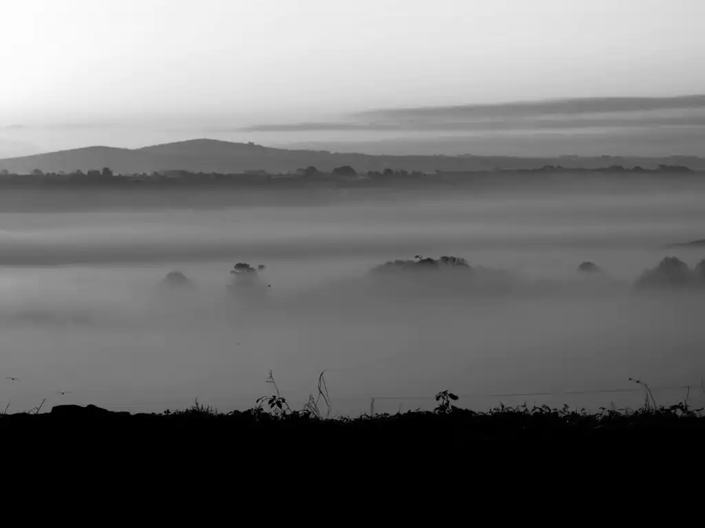 Black and white photo of misty hills overlooking Carbis Bay in Cornwall, creating a serene and atmospheric landscape.
