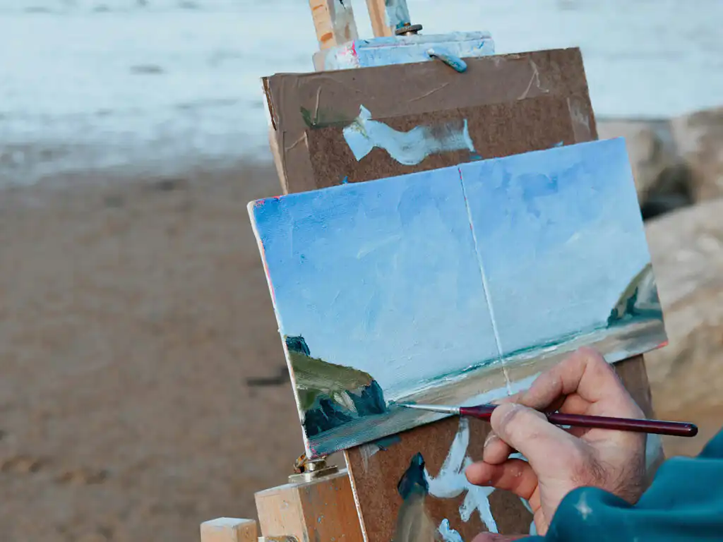 A person painting on Mawgan Porth Beach, capturing the vibrant scenery and artistic spirit of the coastal landscape, a great piece of Mawgan Porth art.
