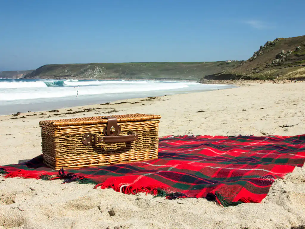 A woven picnic basket rests on Mawgan Porth Beach, perfect for enjoying food and drinks by the ocean.