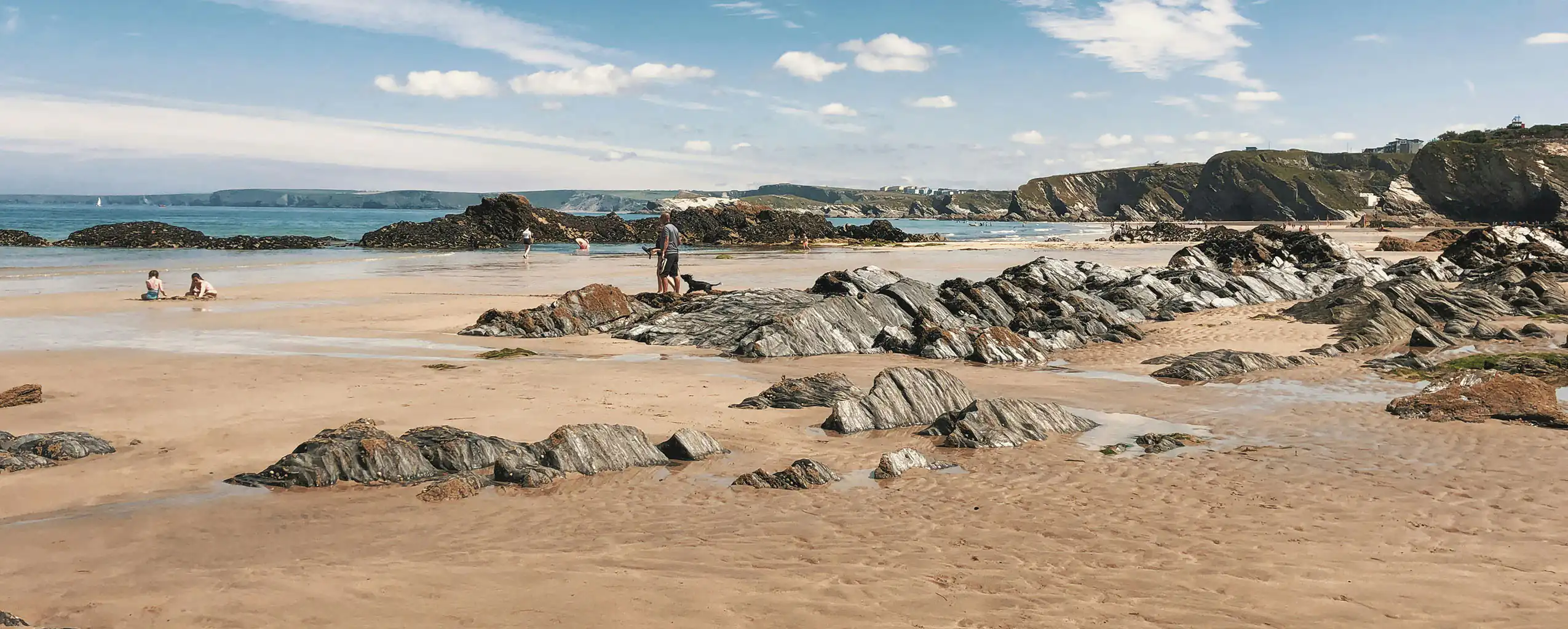 A scenic rocky beach in Newquay, featuring sandy areas, scattered rocks, and gentle waves lapping at the shore, great for building your appetite before exploring Newquay's Food and Drink.