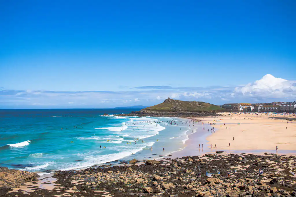 Porthmeor Beach with a sandy shore, ocean waves, and distant rocky hill, a family-friendly beach in West Cornwall.
