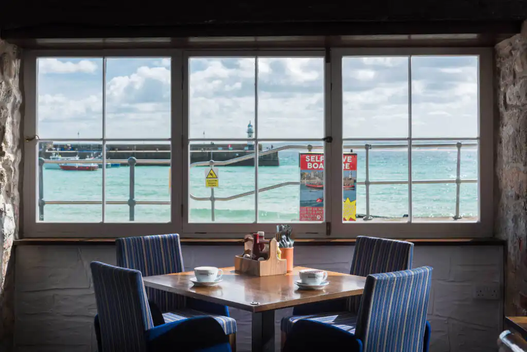 A cosy table with chairs by a window, showcasing a stunning ocean view at The Lifeboat Inn in St Ives, one of the best dog-friendly pubs in West Cornwall.