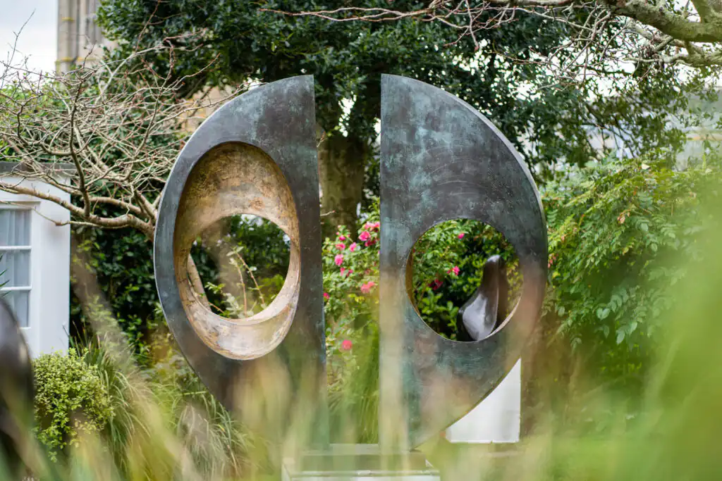 A large metal sculpture stands prominently in the Barbara Hepworth Sculpture Garden, surrounded by lush greenery, one of the best gardens in Cornwall.