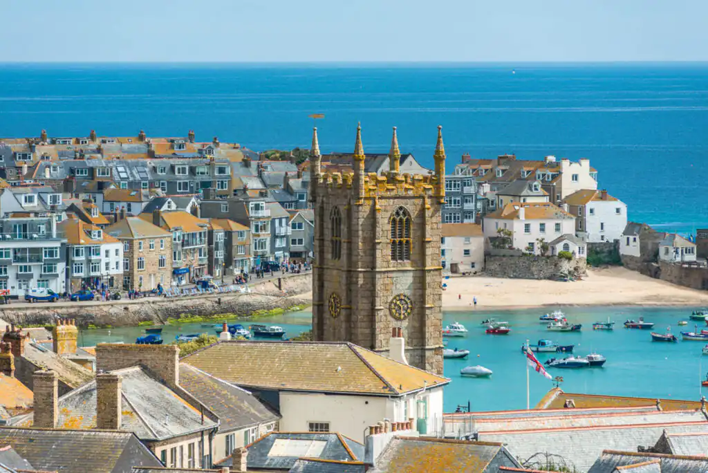 A scenic view of St Ives Harbour, featuring boats and a church, showcasing the charm of the town, home to the St Ives School of Painting.