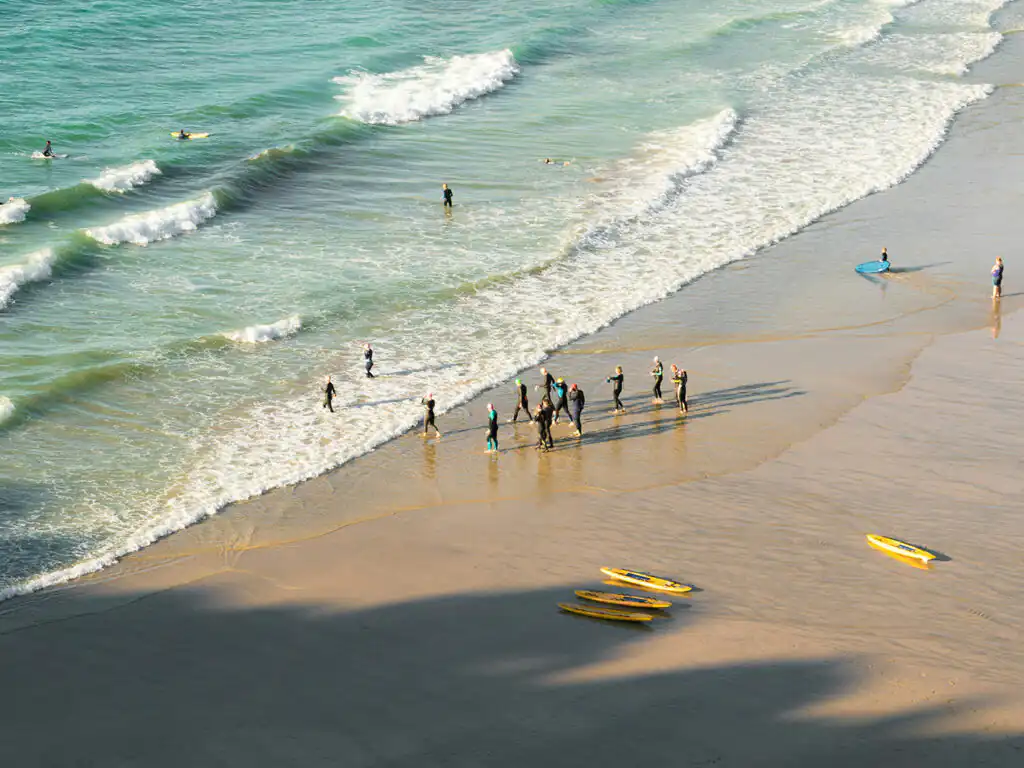 A lively beach scene at St Agnes with surfers and swimmers enjoying the sun and surf, surrounded by colorful surfboards, a great thing to do in St Agnes.