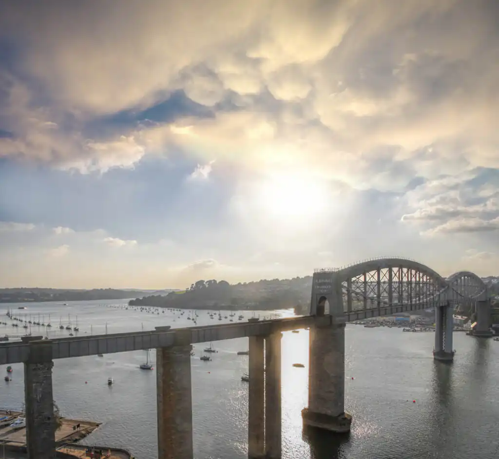 A picturesque bridge over the River Tamar, the starting point of Cornwall's scenic rail journeys, surrounded by lush landscapes.