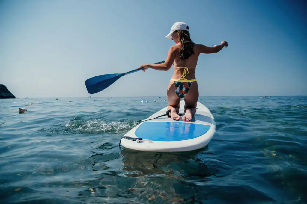 A woman in a bikini glides on a paddle board, embracing the thrill of paddleboarding in Cornwall's beautiful waters, a truly great activity for adventure seekers in Cornwall.