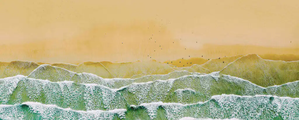 Aerial view of Carbis Bay Beach, featuring waves and birds soaring over the vibrant ocean, a great location for Cornwall holiday cottages.