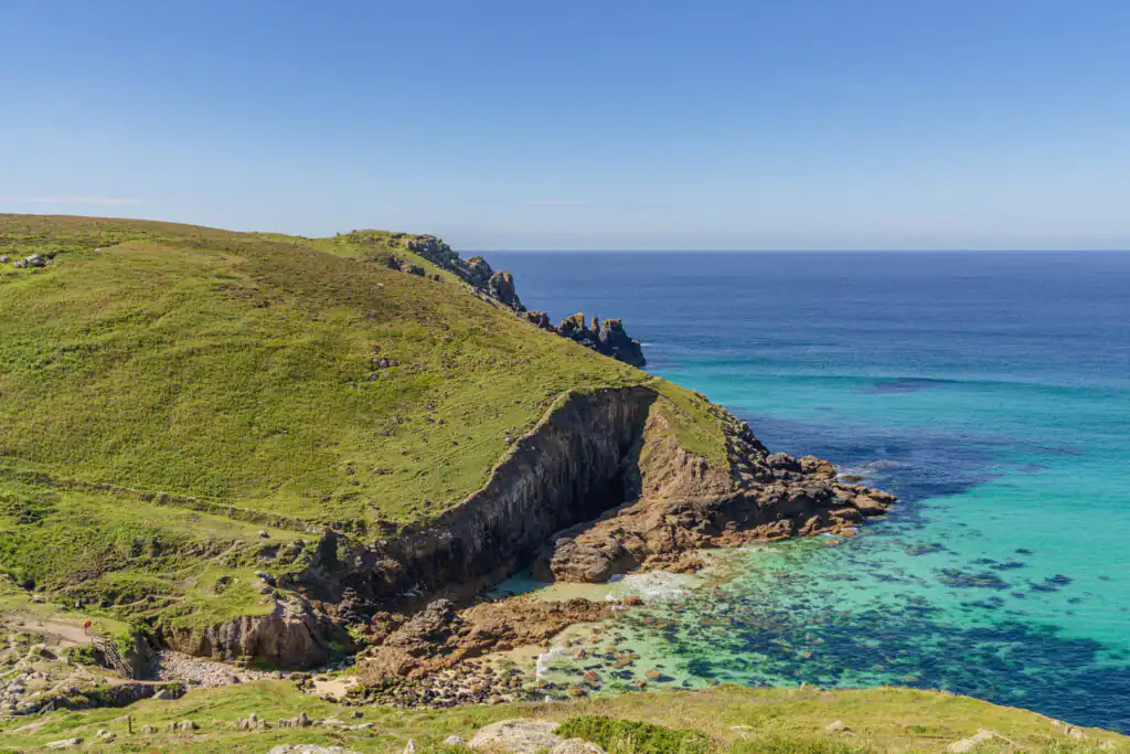 Grassy hillside overlooking a small body of water, capturing the serene beauty of Nanjizal Beach in Cornwall, a great thing to do in Summer in Cornwall.