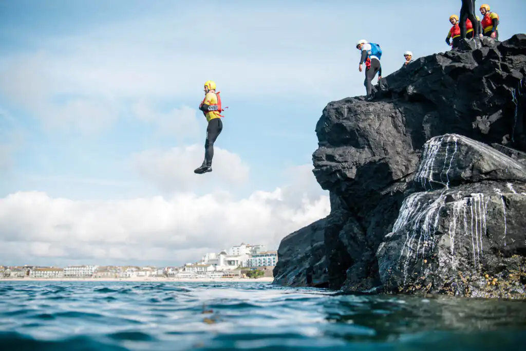 A man leaps off a cliff into the ocean, showcasing the thrill of cliff jumping in St Ives, a great thing to do in Summer in St Ives.