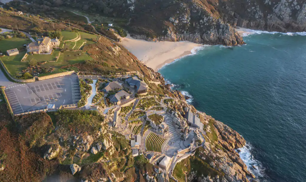 Overhead shot of a cliffside Minack Theatre overlooking the ocean, showcasing the breathtaking landscape of Cornwall, a great thing to do in Cornwall during the summer.