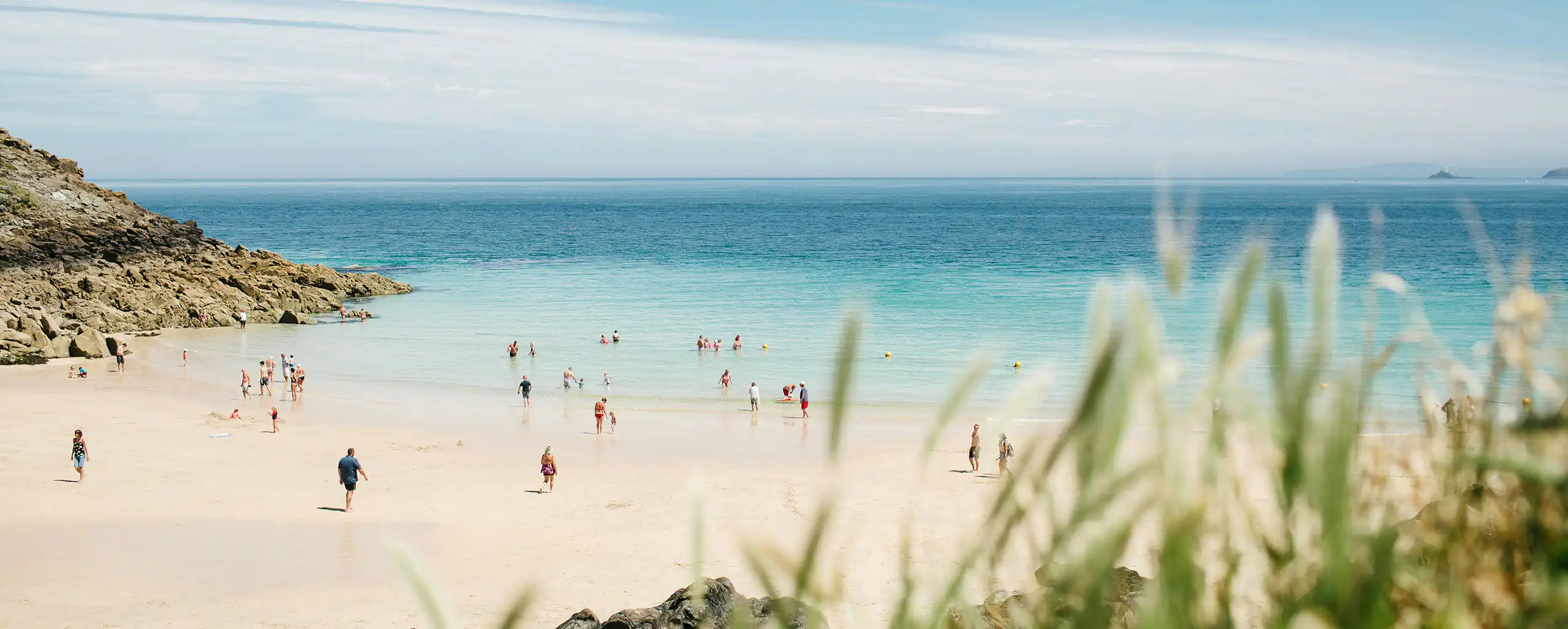 A lively group of people enjoying a sunny day at Porthgwidden Beach, with the sparkling water in the background, discover this location after browsing your guest booking terms and conditions.