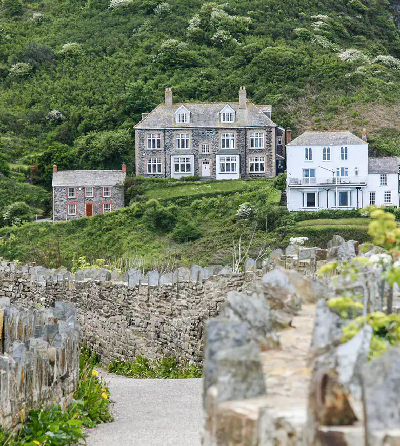 A charming stone wall with a path leading to the cottages used when filming 'Doc Martin' in Port Isaac, surrounded by lush greenery.