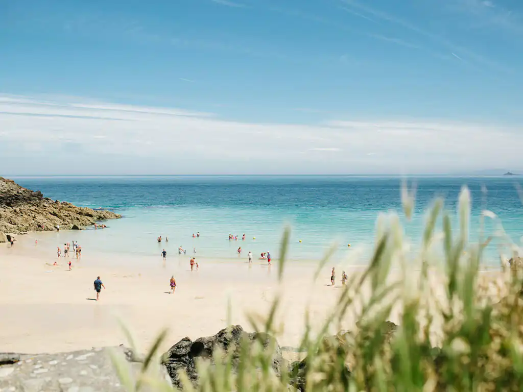 People relax and enjoy the sunny day at Porthgwidden Beach in St Ives, surrounded by golden sand and clear blue water, it also has many great food and drink options.