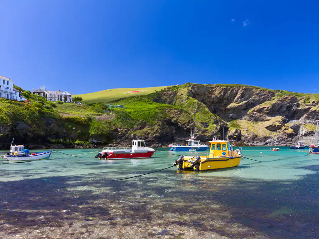 Boats gently bob in Port Isaac harbour under a bright blue sky with fluffy white clouds, a great thing to do in Port Isaac.
