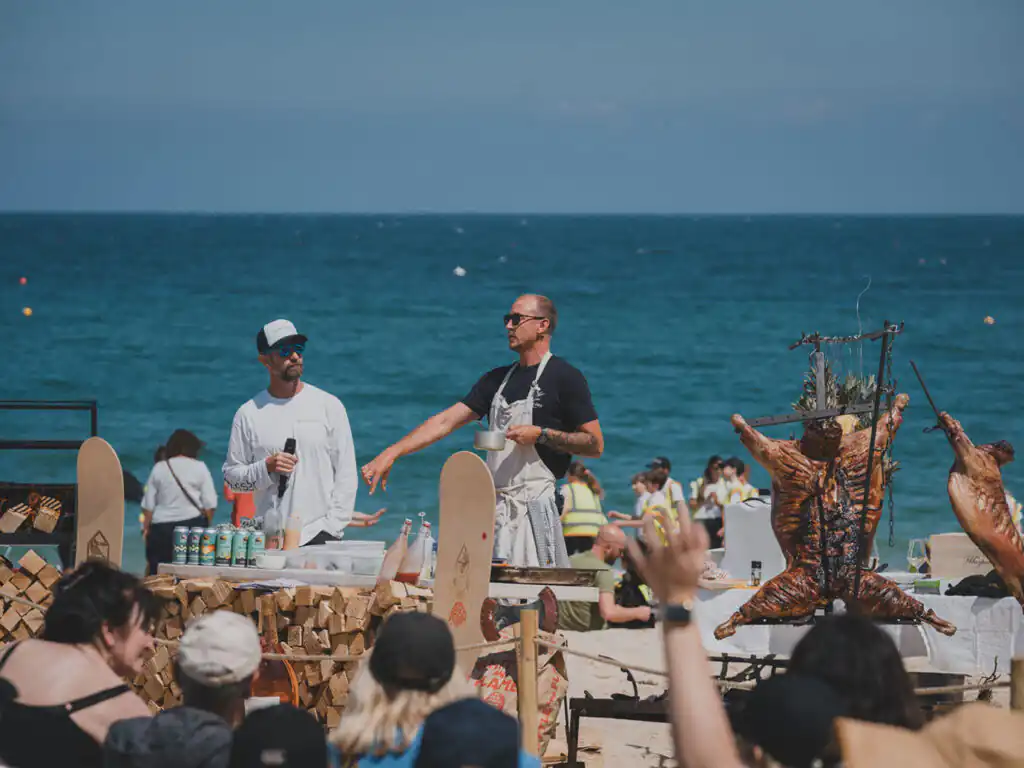 Two chefs demonstrate cooking on a beach during the St Ives Food Festival, with an audience watching eagerly, don't miss out on all of the food and drink.