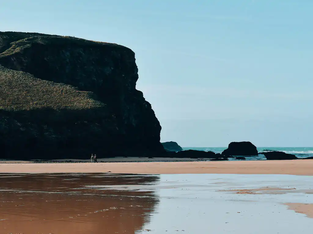 A person strolls along Mawgan Porth Beach, with waves gently crashing in the background, a place with lots of arts and heritage.