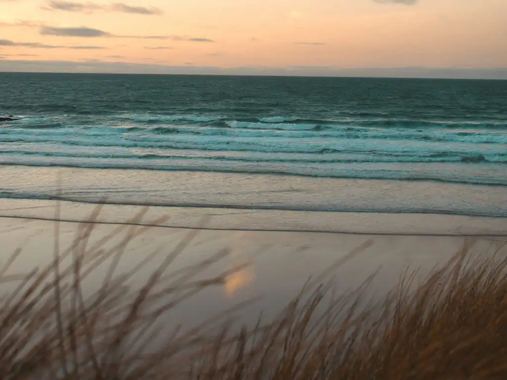 Gwithian Beach, with golden sands and a clear blue sky in the background, close to many food and drink options in Hayle.