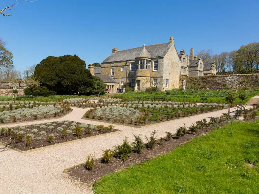 A scenic garden with a stone path leading to Trerice Manor House, surrounded by lush greenery near Mawgan Porth, a great piece of arts and heritage.