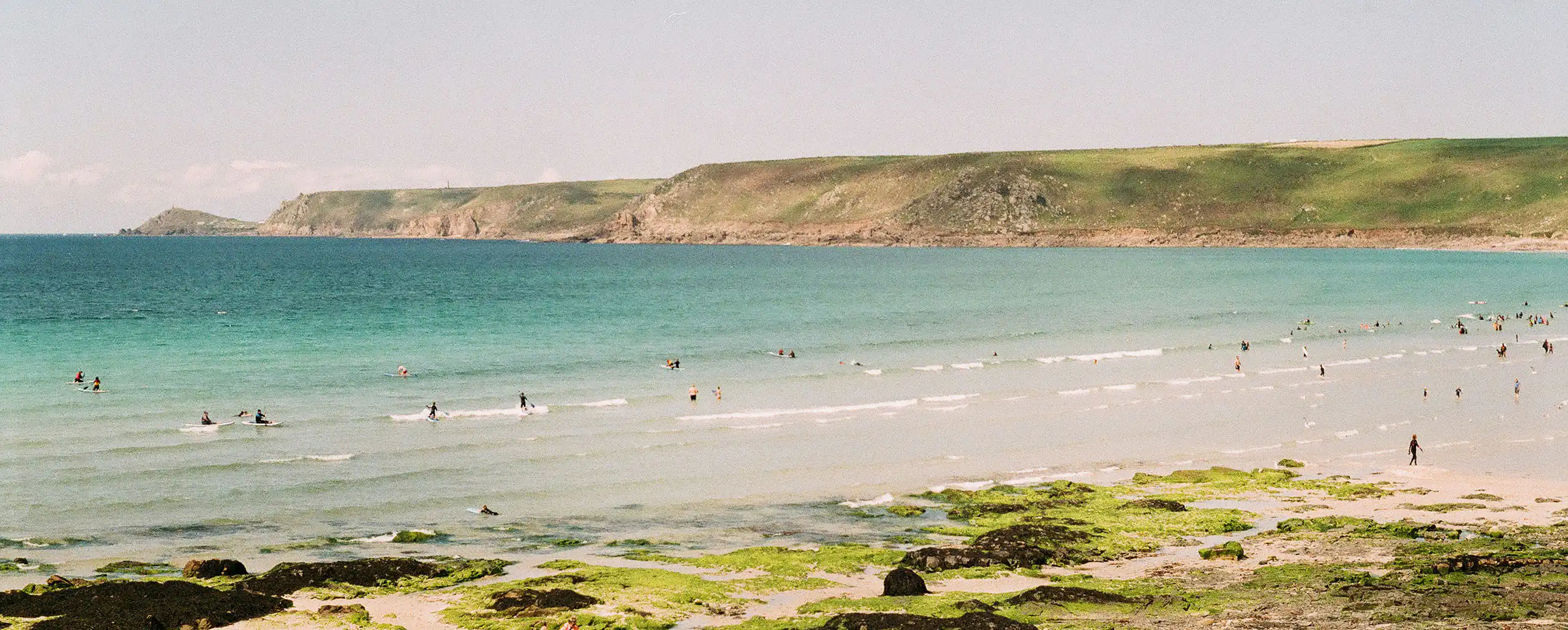 Sennen Cove Beach in Cornwall, featuring people swimming in the water and others relaxing on the sandy shore,  discover this location after browsing our terms and conditions.