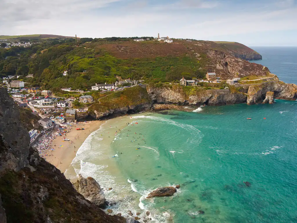 A picturesque coastal scene of St Agnes Beach, featuring golden sands and the charming town nestled along the shore, don't forget to explore St Agnes' food and drink options.