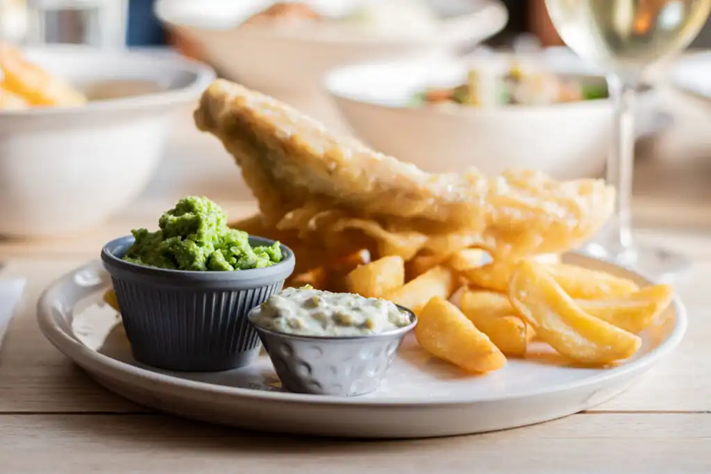 A delicious plate of golden fish and chips served with tartar sauce, set on a rustic wooden table, a great way to enjoy the best fish and chips in Cornwall.