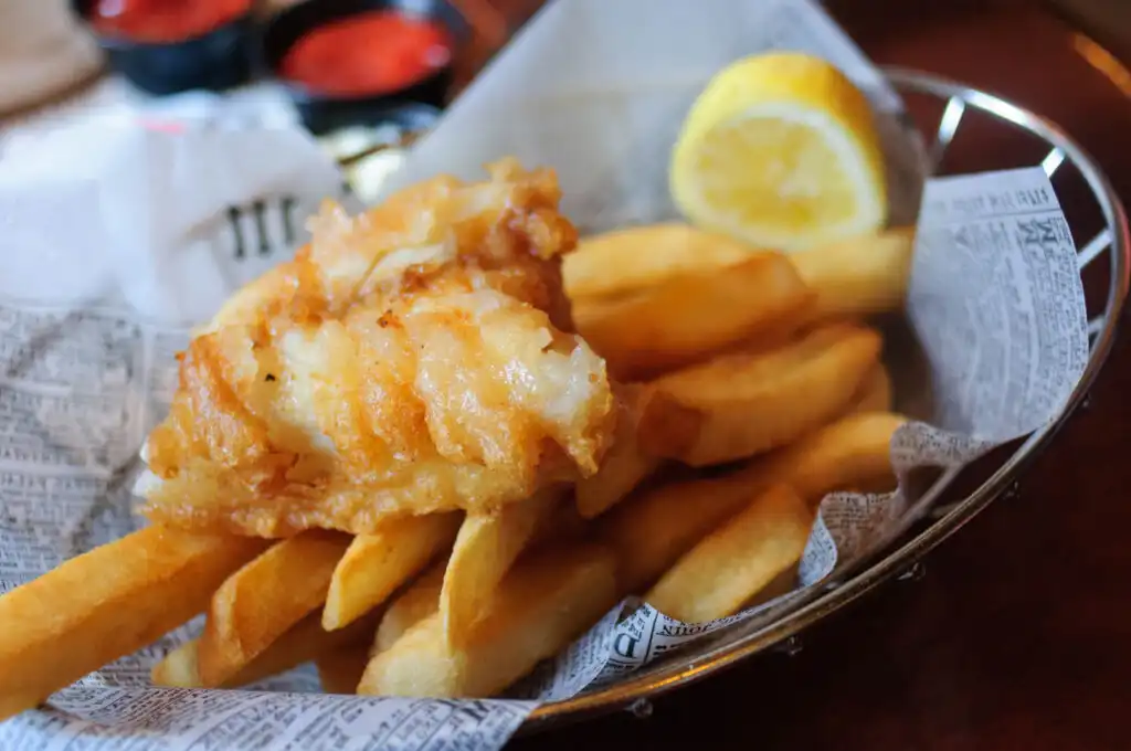 Crispy fish and golden chips served in a basket, garnished with a fresh lemon wedge for a zesty touch, the makeup of the best fish and chips in Cornwall.