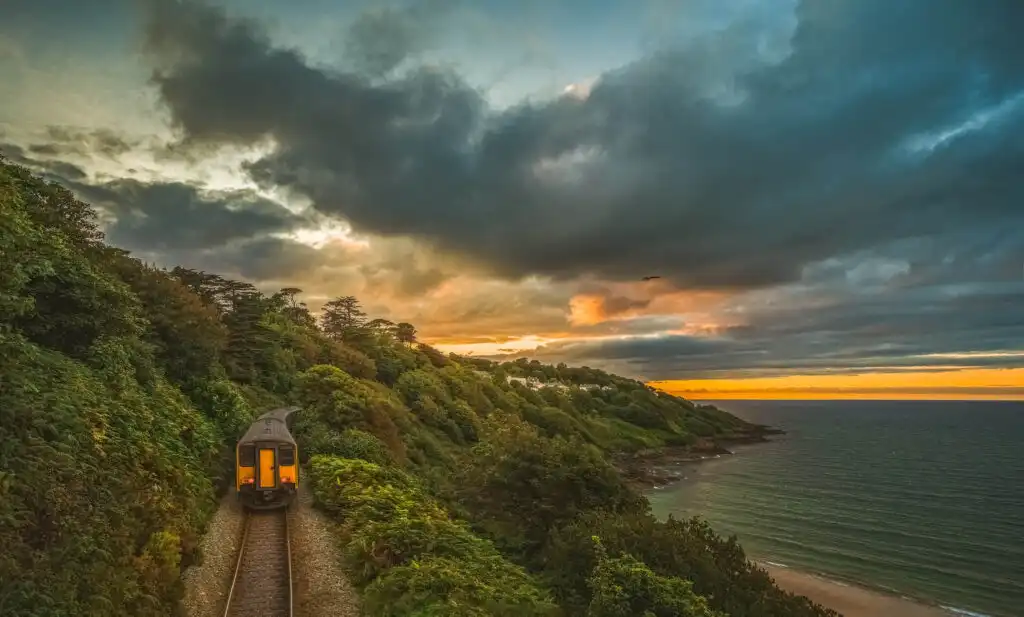 A train glides along the tracks beside the ocean, showcasing the scenic beauty of Carbis Bay, a great idea for transport when planning a holiday in Carbis Bay.