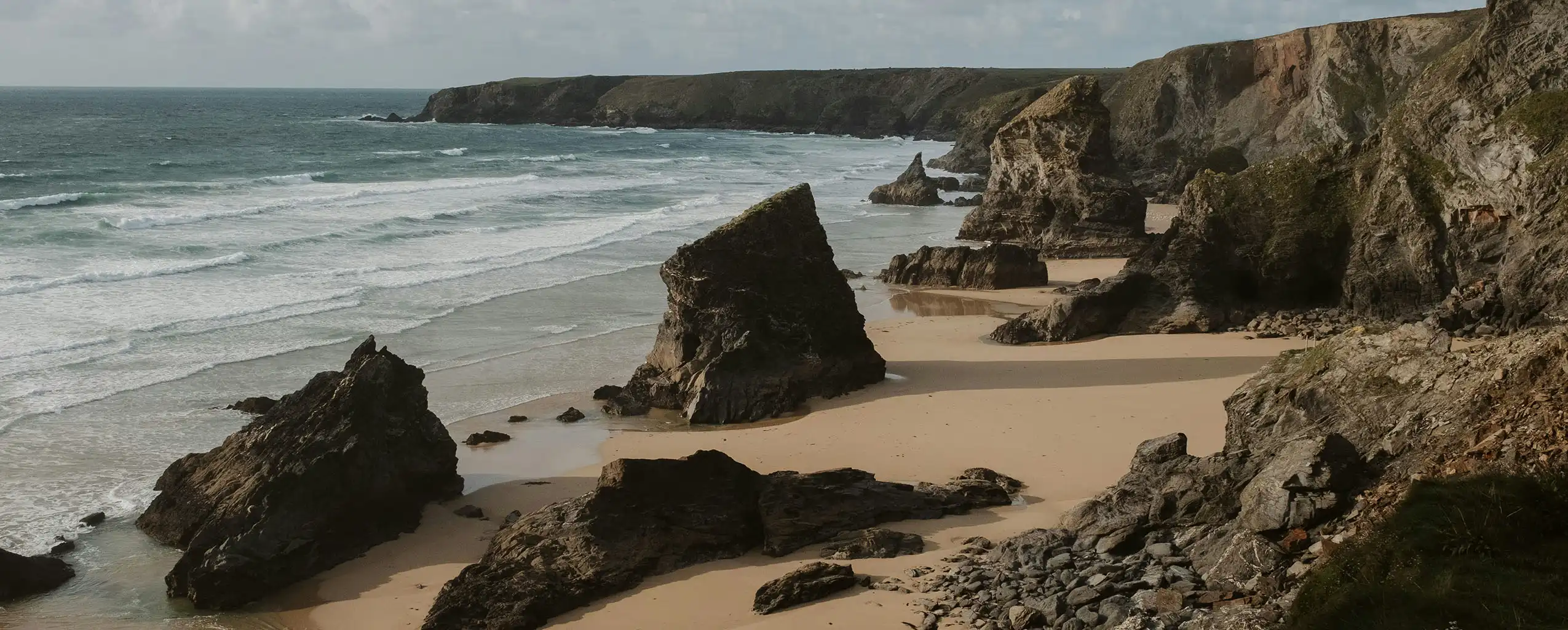 Scenic view of Bedruthan Steps, showcasing sandy beach and towering cliffs under a clear blue sky, a great place to visit from a luxury holiday cottage in Cornwall.