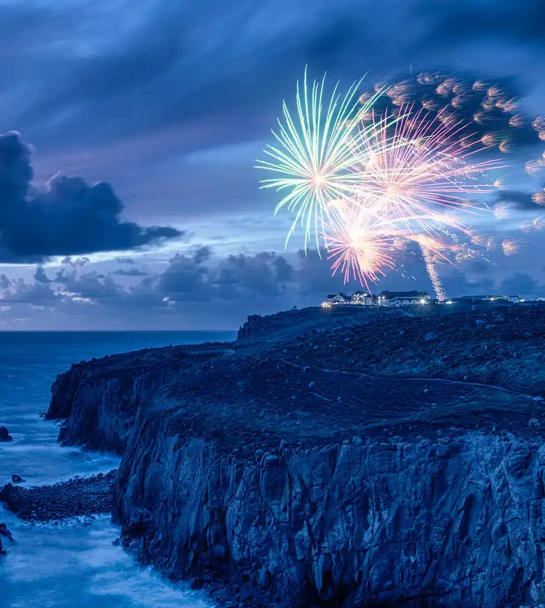 A stunning rock formation at Land's End, illuminated by vibrant fireworks celebrating New Year's Eve in Cornwall, just one of many fantastic things to do from one of Cornish Escapes' Cornwall holiday cottages.