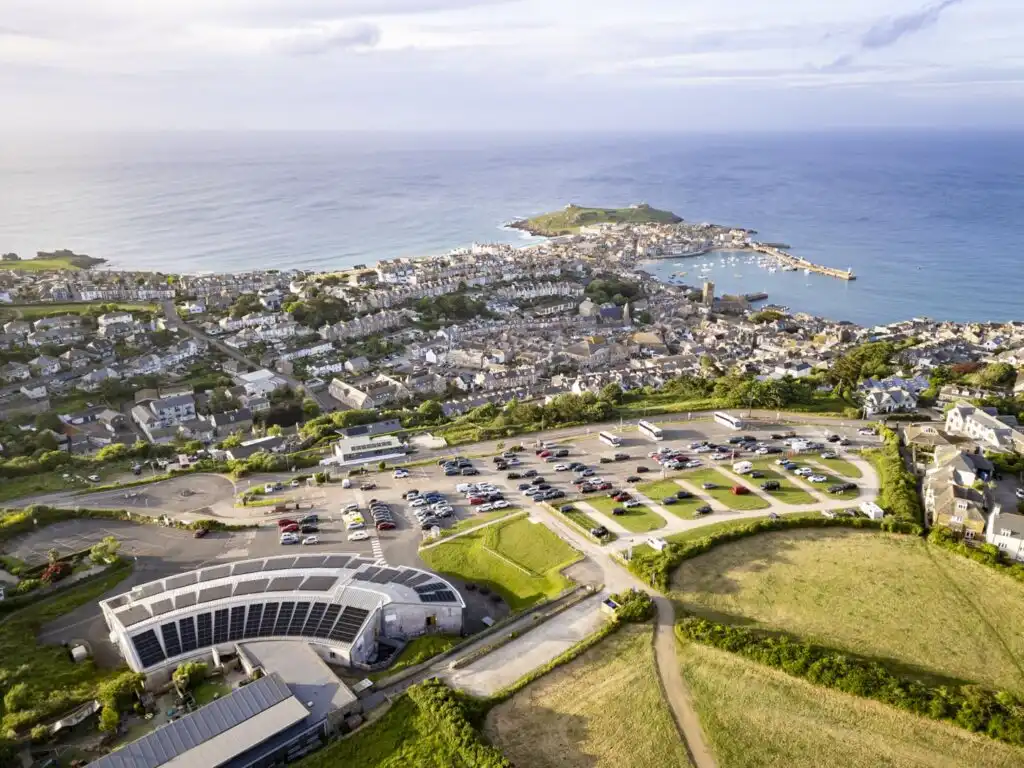 Overhead shot of Trenwith Car Park in St Ives, the largest parking option in St Ives, highlighting the bustling town alongside the beautiful beach and ocean.