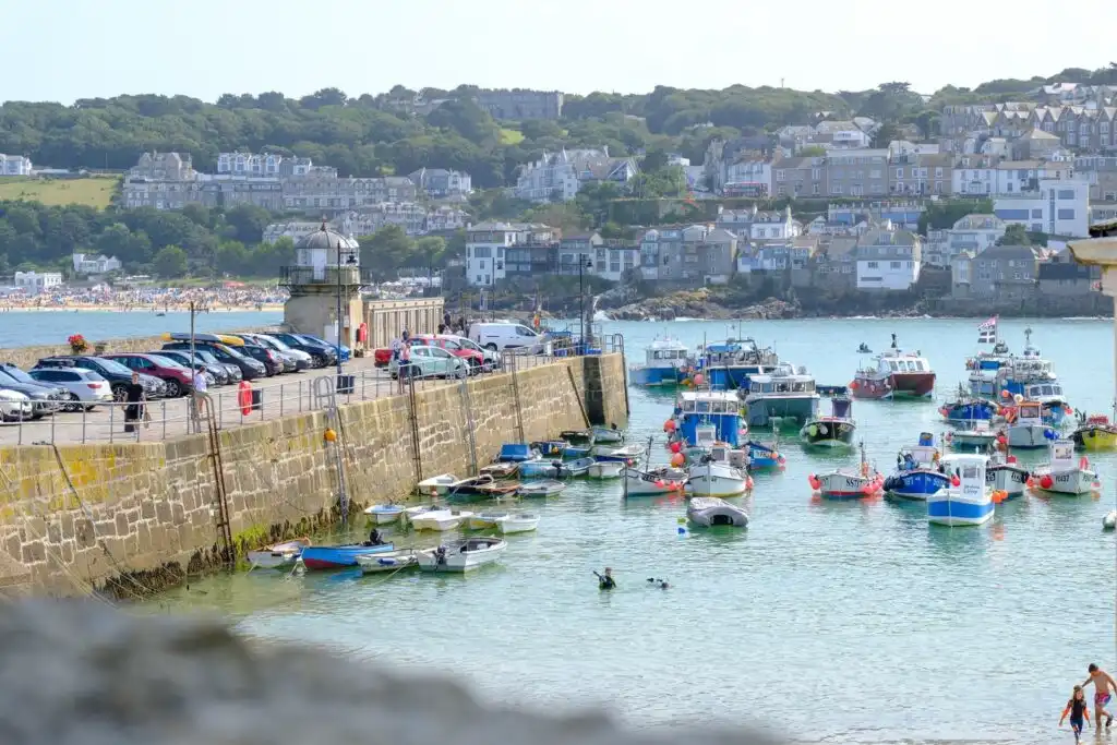 A bustling St Ives Harbour filled with colourful boats and people enjoying the vibrant waterfront atmosphere, the pier offers parking in St Ives.