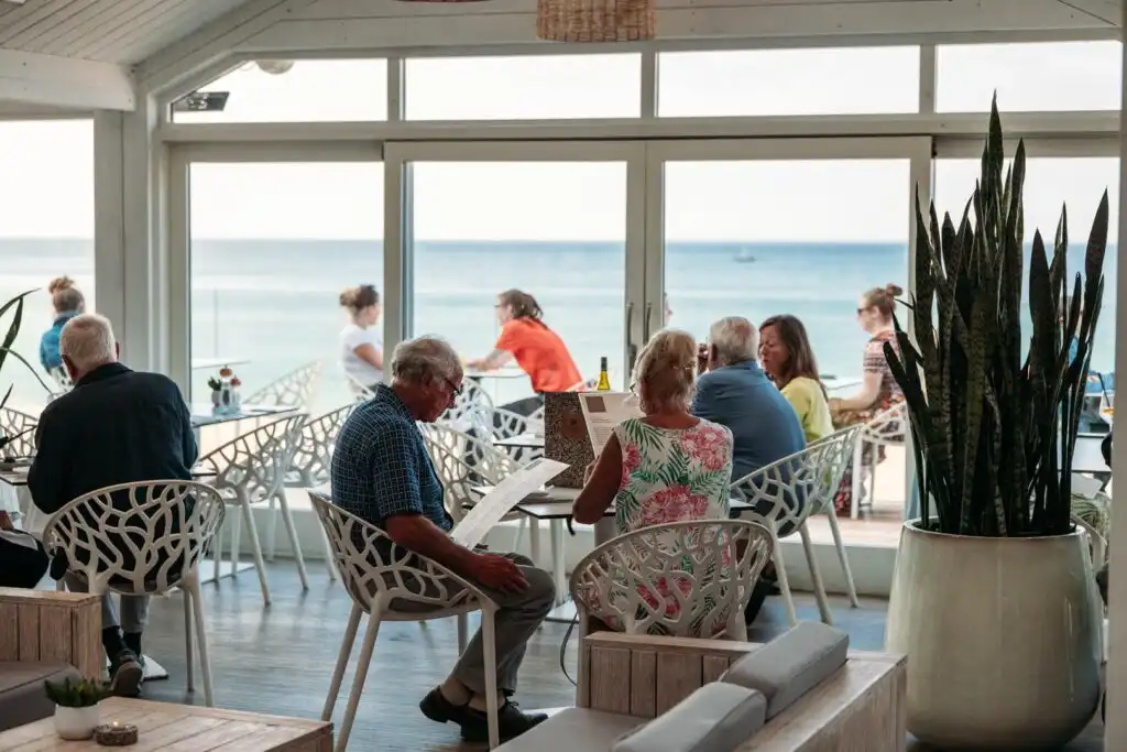 Guests enjoying meals at outdoor tables in the vibrant Carbis Bay Beach Club, with a scenic beach view in the background, a great place for food and drink in Carbis Bay.