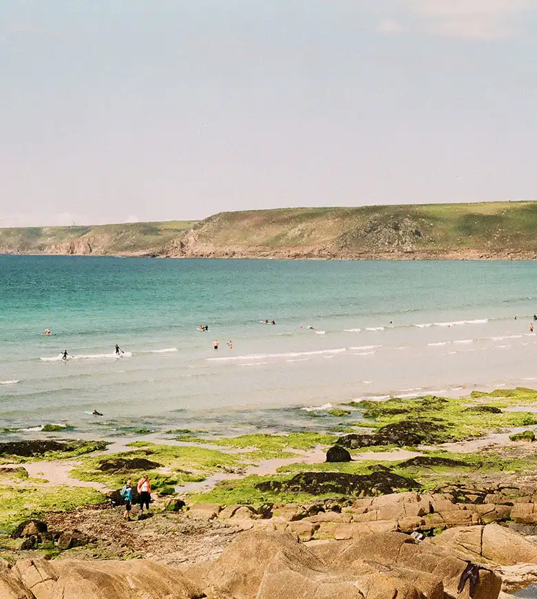 A group of friends relaxes on rocks by the ocean at Sennen Cove, enjoying the scenic beauty of Cornwall. a great place to explore from a Cornwall holiday cottage